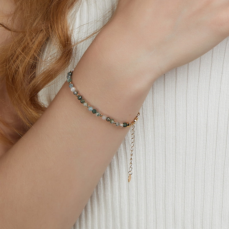 Person wearing gold - toned beaded bracelet: Bracelet on wrist, white top, showcasing the accessory.