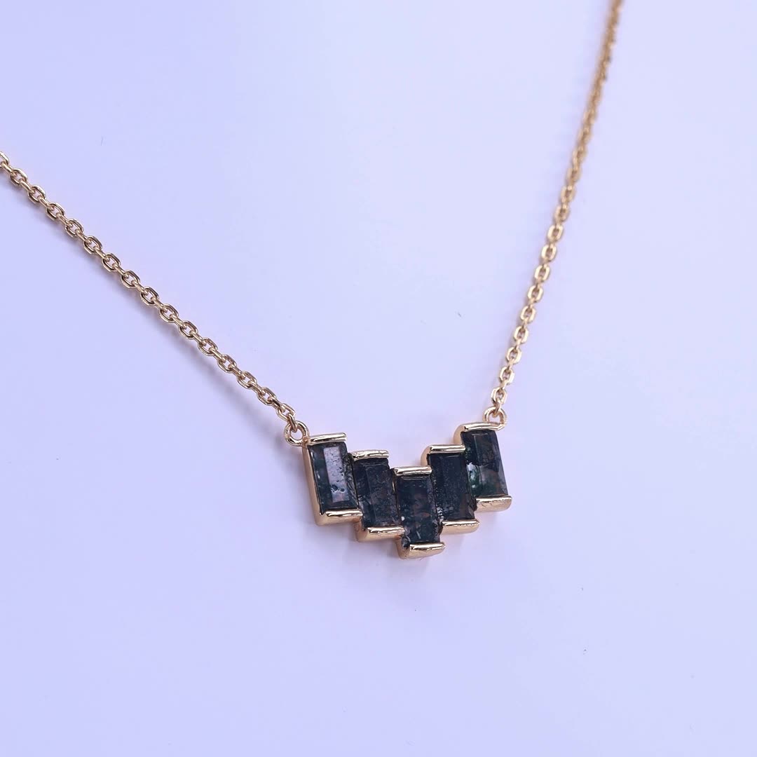 Gold - toned necklace: Geometric pendant with baguette moss agate stones, on a light purple background.