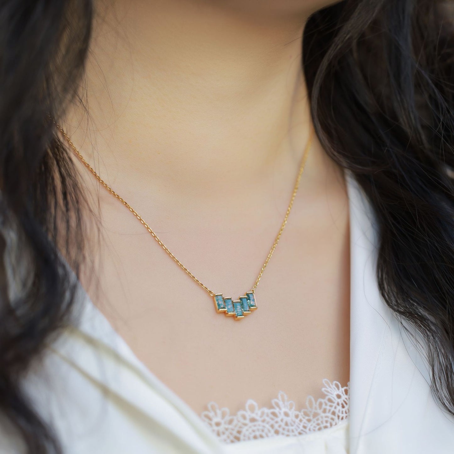 Close - up of a person wearing gold - toned necklace: Geometric pendant with rectangular moss agate stones, showcasing elegant style.