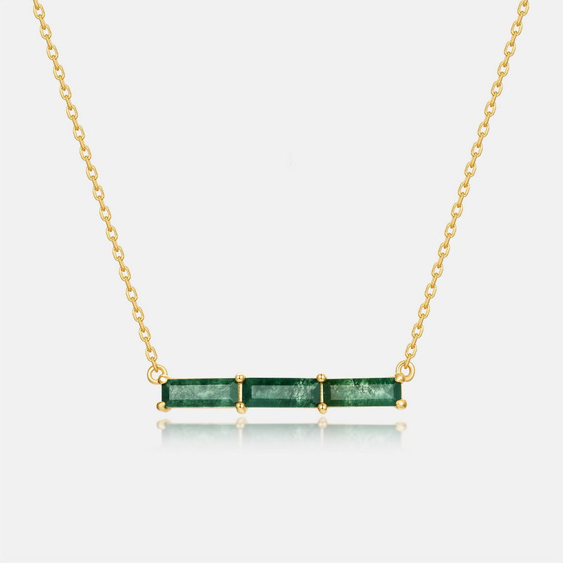 Gold - toned necklace: Horizontal bar pendant with three emerald - cut green stones on gray background.
