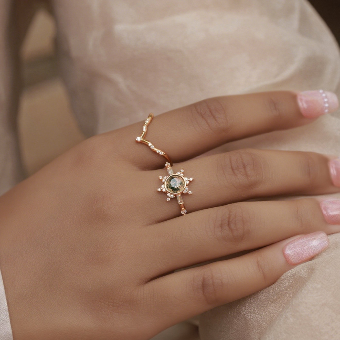 Gold - toned ring set: A sun - shaped moss agate ring and a curved crystal - studded ring, shown on a hand with light pink nails.