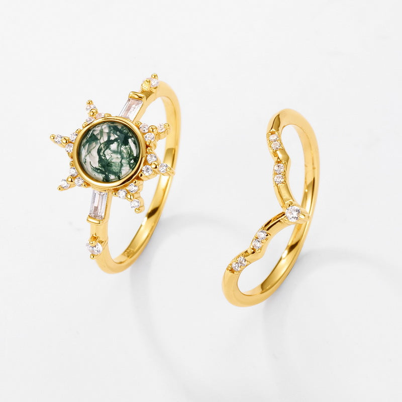 Gold - toned ring set: A sun - motif moss agate ring and a curved crystal - encrusted ring, isolated on a white background.