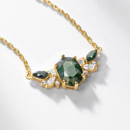 Gold necklace with an oval moss agate center, flanked by green gemstones, opals, and clear crystals, on a white background.