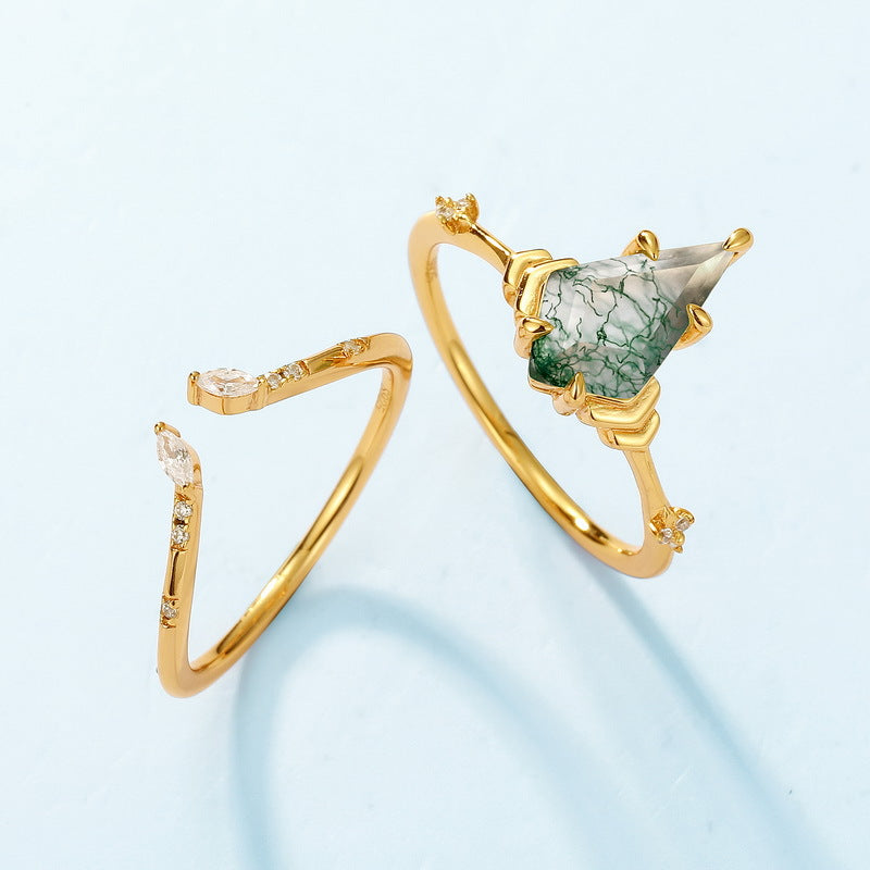 Two gold rings: One with a teardrop moss agate, the other open - band with crystals, placed on a light blue background.