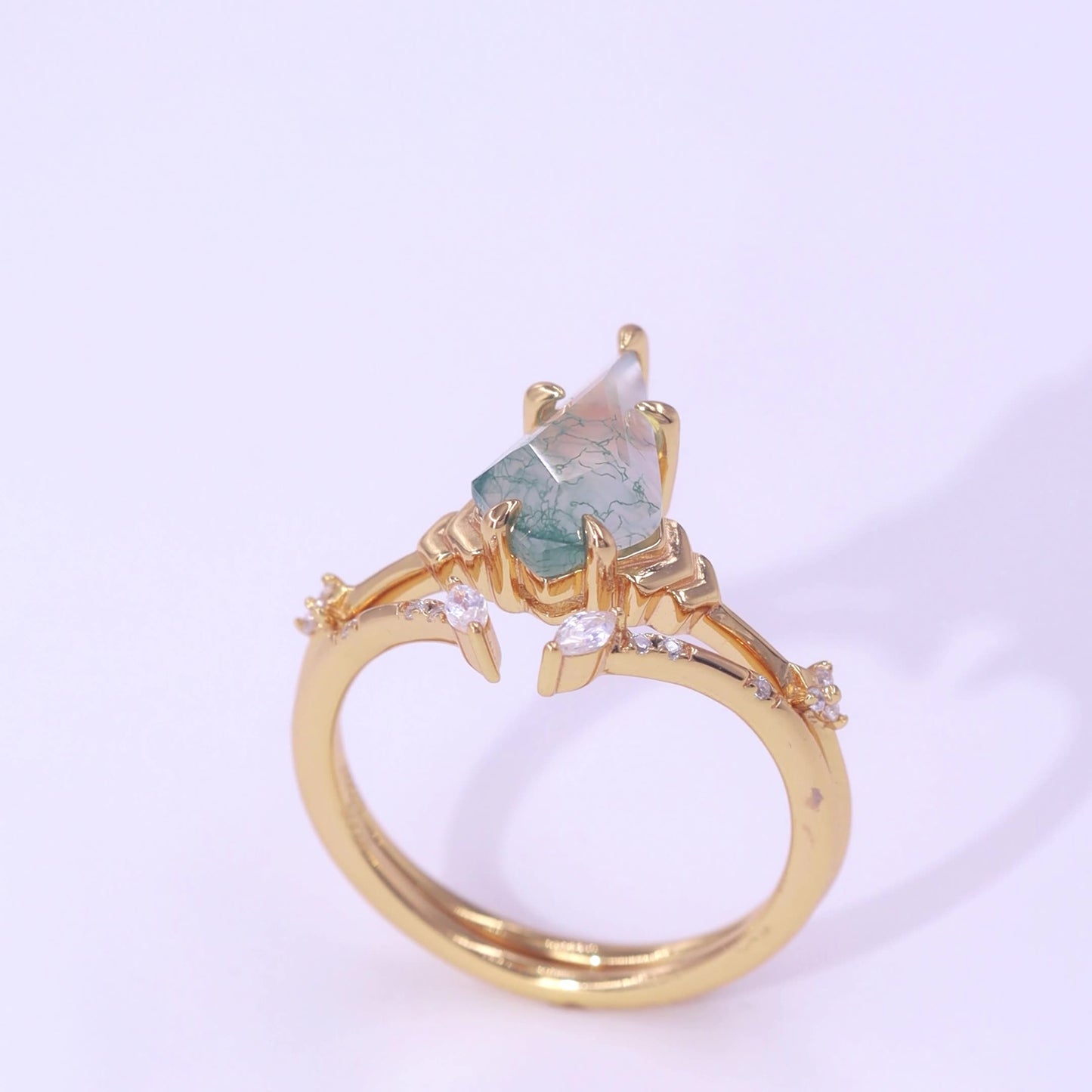 Gold ring featuring a teardrop moss agate, crystal accents on branches, displayed on a light pink background.