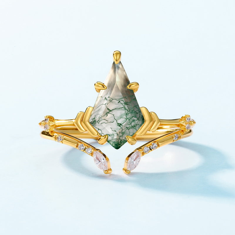 Gold ring stack: Teardrop moss agate ring with crystal - lined bands, set against a light blue background.
