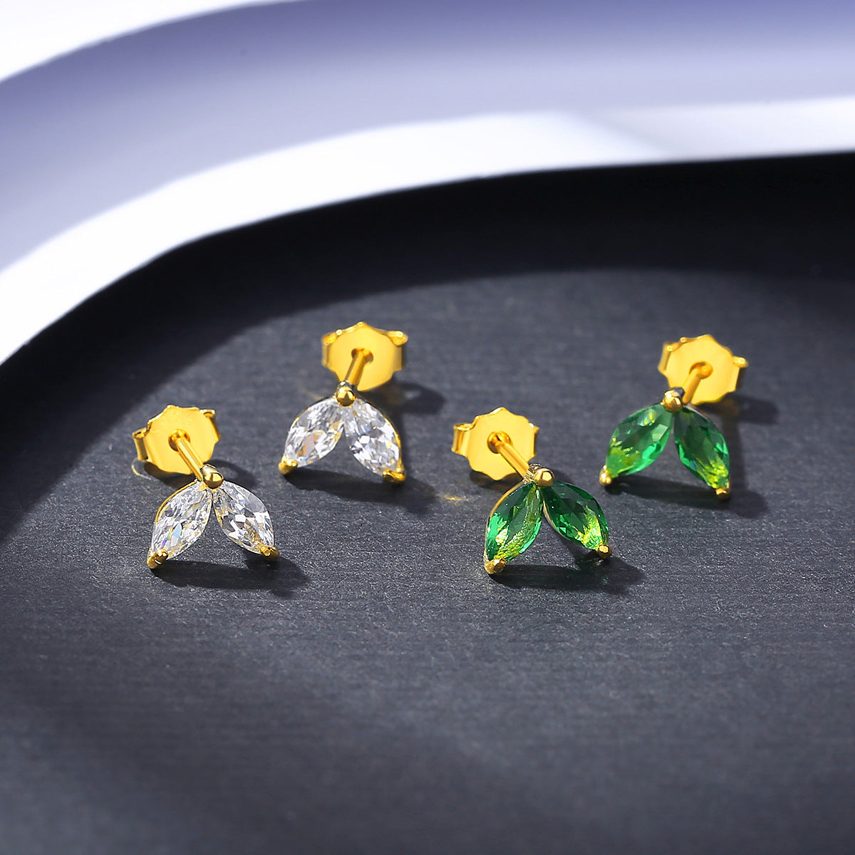 two Pair of yellow gold earrings with marquise clear and green cubic zirconia details on a dark surface