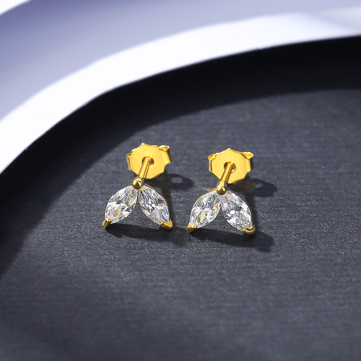 Gold earrings with clear gemstones on a dark surface