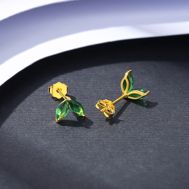 Gold earrings with green gemstones on a dark surface