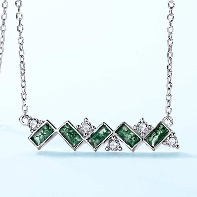 Extreme close - up of silver - toned necklace pendant: Horizontal pendant, green moss agate stones, clear crystal accents, isolated on white, emphasizing details.