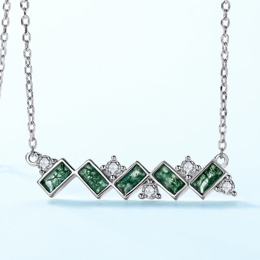 Extreme close - up of silver - toned necklace pendant: Horizontal pendant, green moss agate stones, clear crystal accents, isolated on white, emphasizing details.
