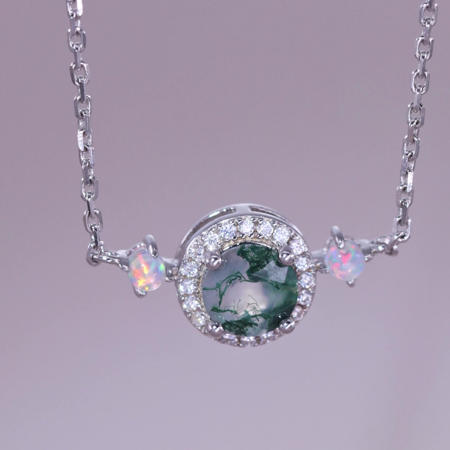 Extreme close - up of silver - toned necklace pendant: Circular moss agate stone, crystal halo, opal - like accents