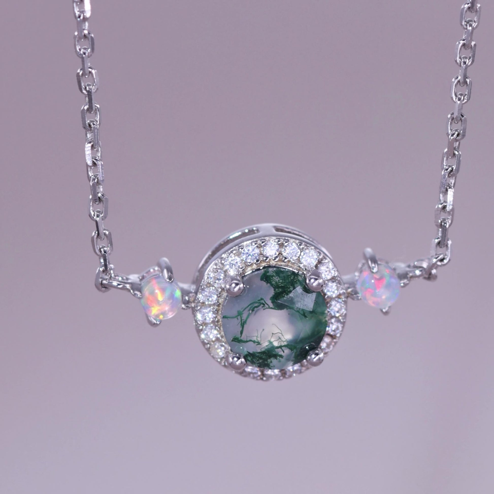 Extreme close - up of silver - toned necklace pendant: Circular moss agate stone, crystal halo, opal - like accents