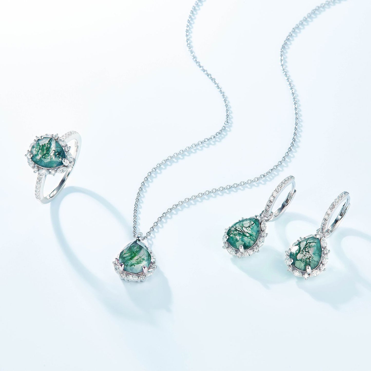 Silver - toned jewelry set: Ring, necklace, earrings, all with teardrop moss agate and crystal halos, isolated on white.