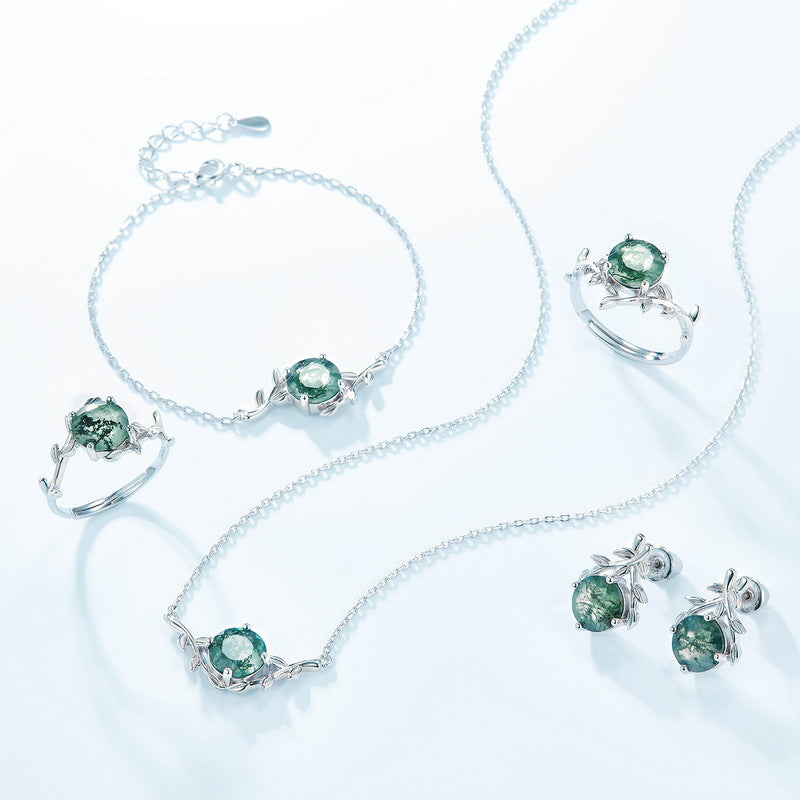 Silver - toned jewelry set: Necklaces, bracelets, rings, earrings, all with round moss agate pendants and leaf - shaped designs, isolated on white.