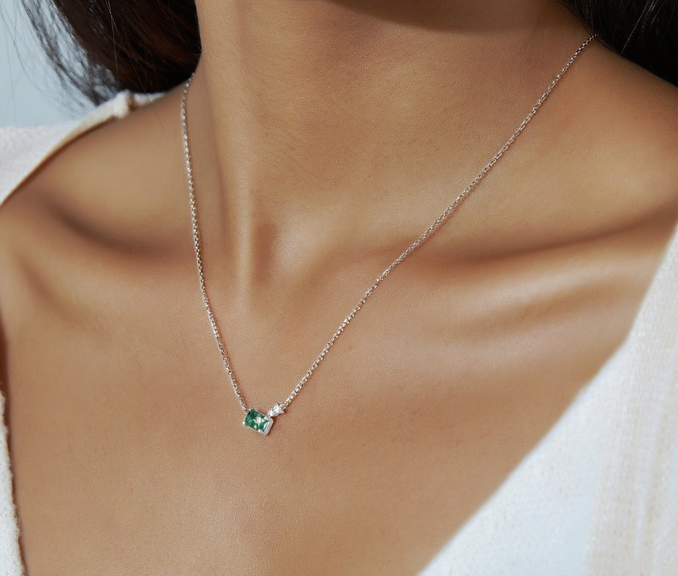 Close - up of a person wearing silver - toned necklace: Rectangular moss agate pendant, small clear crystal accent, showcasing elegant style.