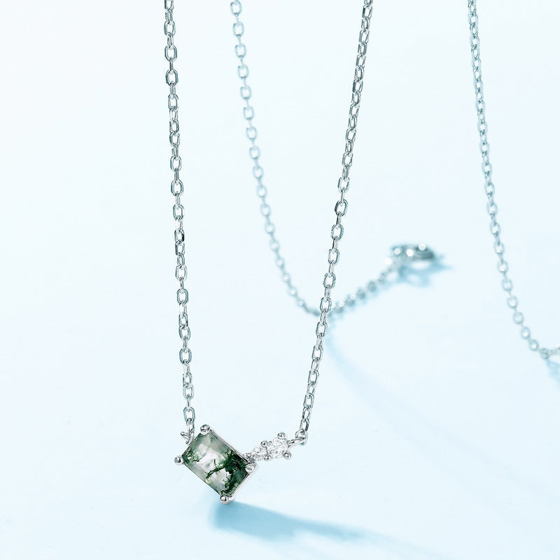 Silver - toned necklace: Rectangular moss agate pendant, small clear crystal accent, isolated on light blue, emphasizing the pendant.