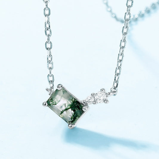Extreme close - up of silver - toned necklace: Rectangular moss agate pendant, small clear crystal accent, isolated on light blue, highlighting intricate details.