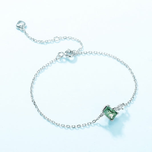 Silver bracelet: Rectangular moss agate, clear crystal accent, chain with heart - shaped extender, light blue background.