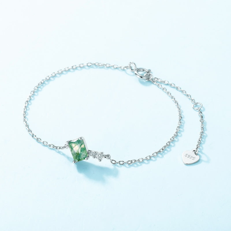 Silver bracelet with a green gemstone on a light blue background