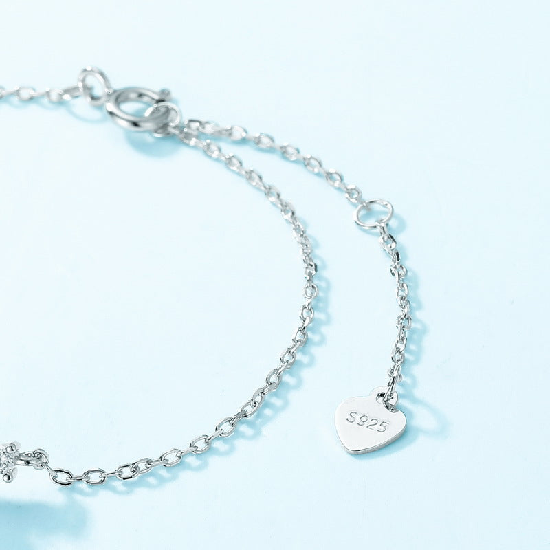 Close - up of silver bracelet extender: “S925” heart tag, light blue background.