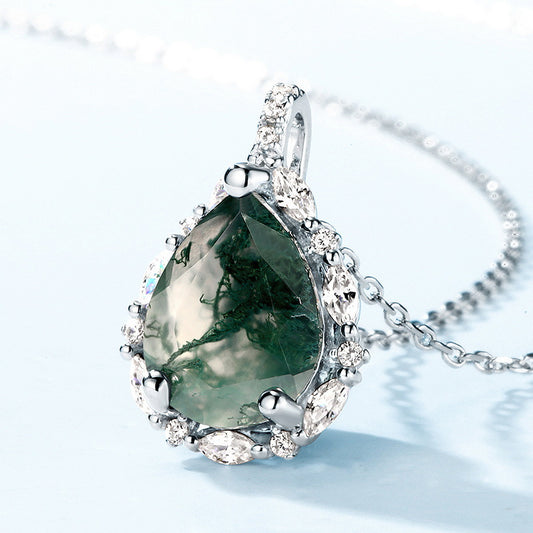 Silver pendant necklace: Teardrop - shaped moss agate, surrounded by clear crystals, light blue background.