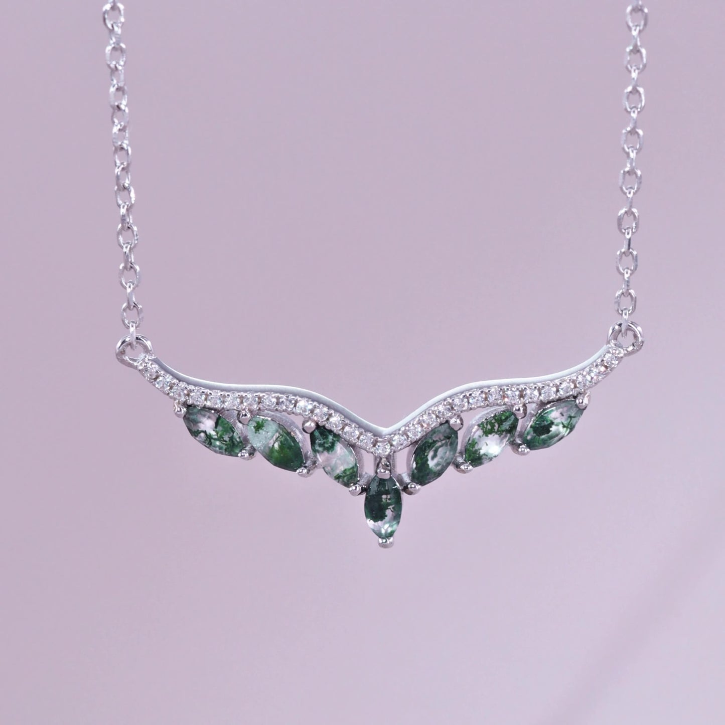 Silver - toned necklace: V - shaped pendant with marquise moss agate stones, crystal accents, on a light purple background.