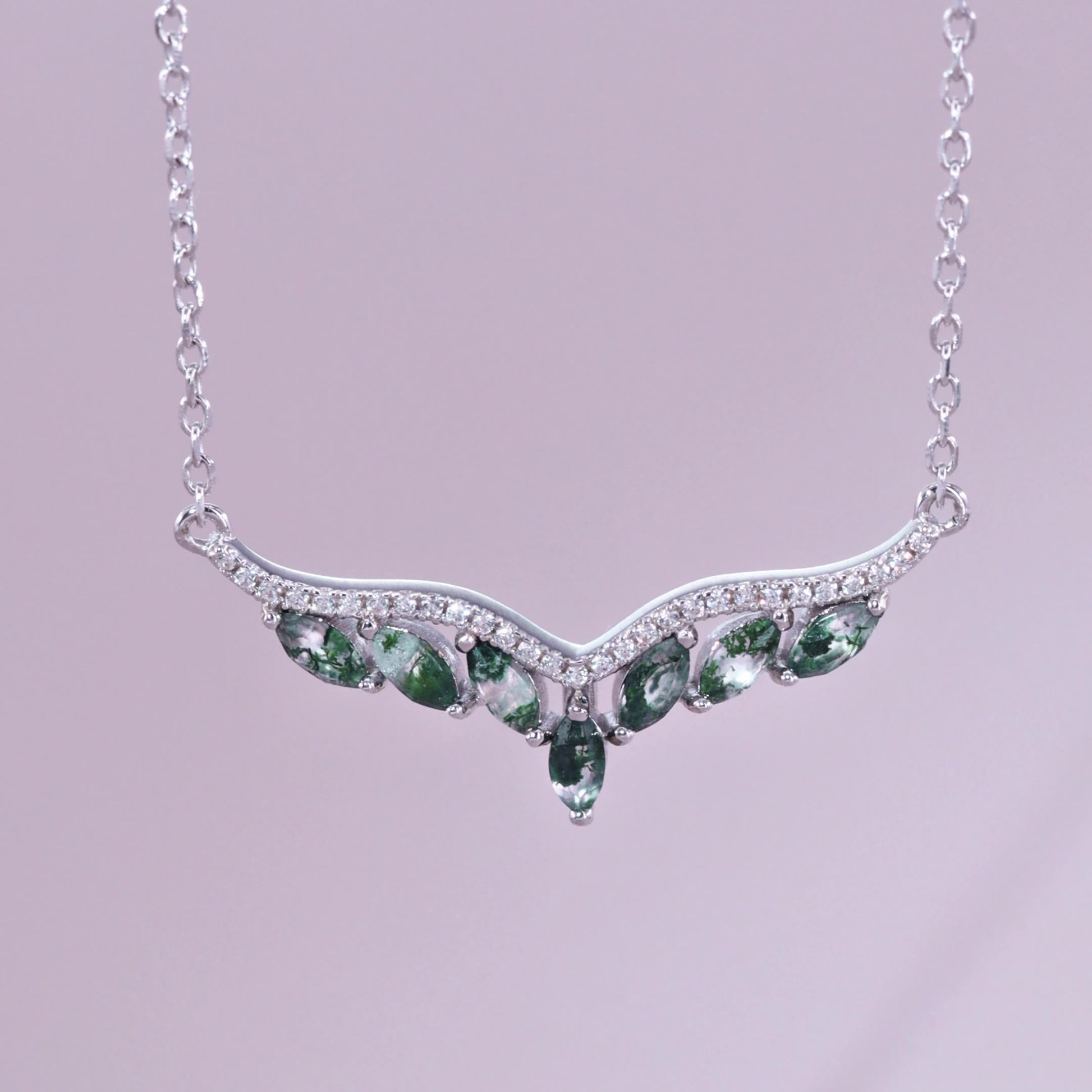 Silver - toned necklace: V - shaped pendant with marquise moss agate stones, crystal accents, on a light purple background.