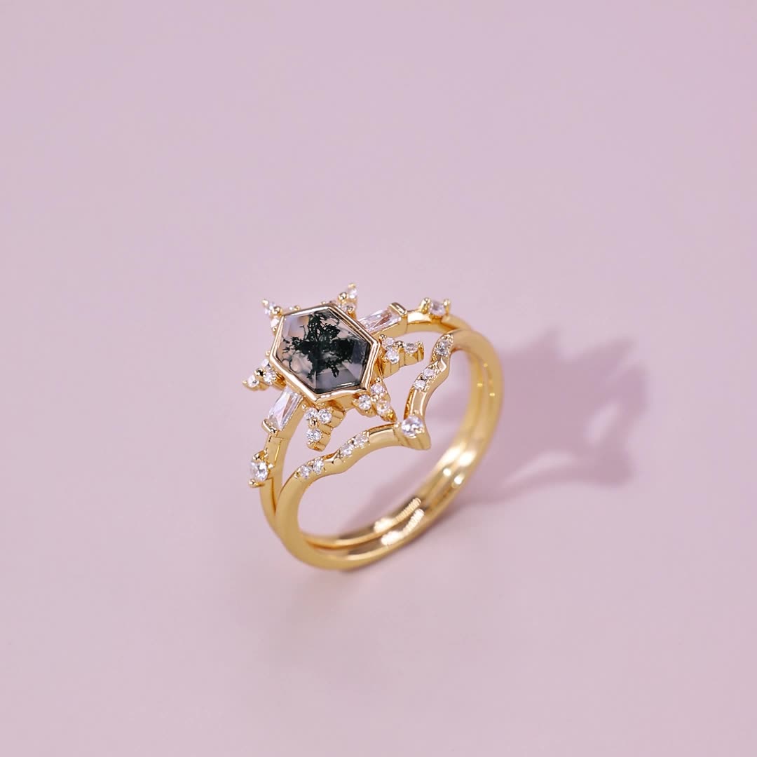 Gold - toned ring set with a hexagonal moss agate, crystal accents, on a light pink background.