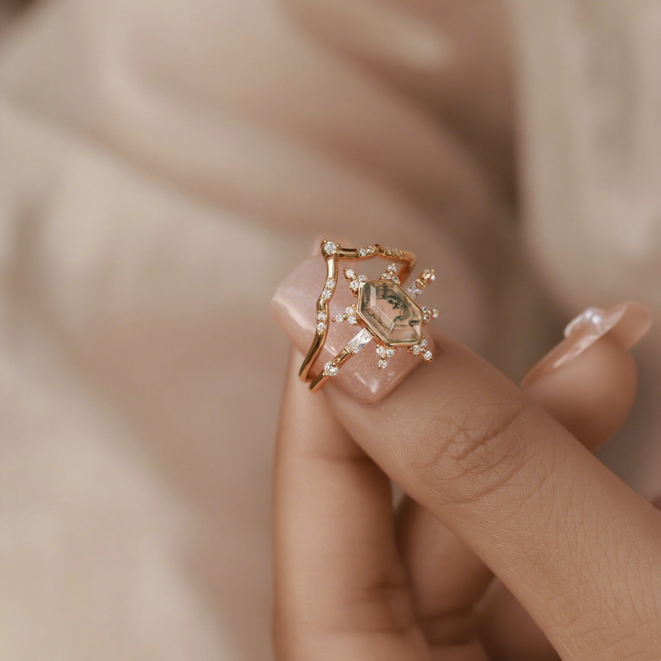Close - up of gold - toned ring set: Hexagonal moss agate ring with crystal - decorated bands, on a light - colored background.