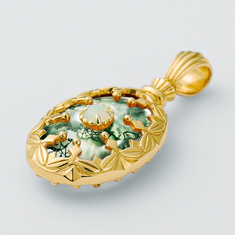 Gold - toned pendant: Oval moss agate stone with central opal, decorative frame, isolated on white.