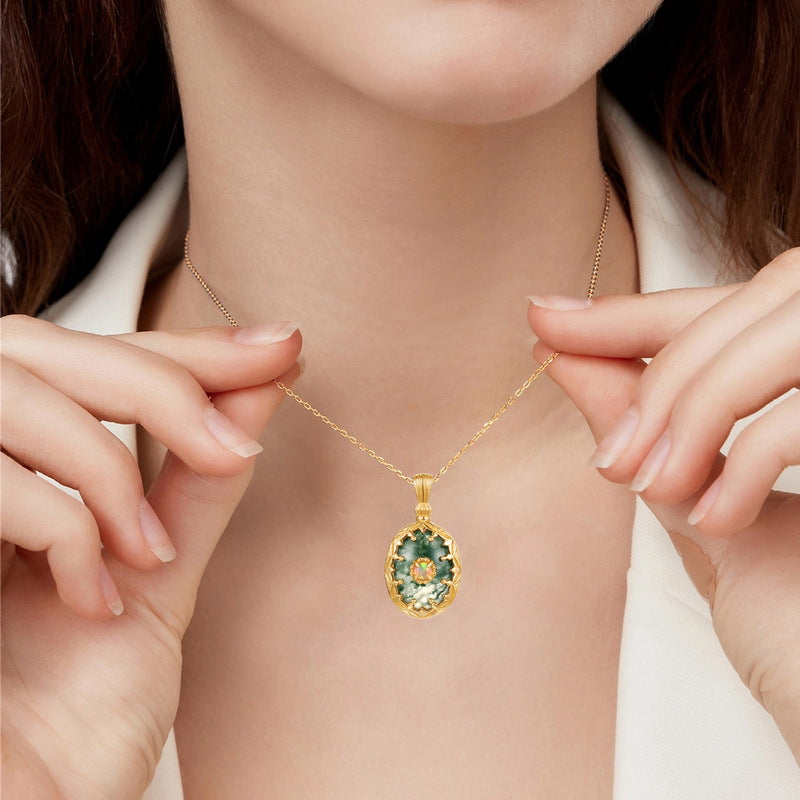 A person wearing a gold - toned necklace: Oval moss agate pendant with central opal, decorative frame, showcasing elegance.