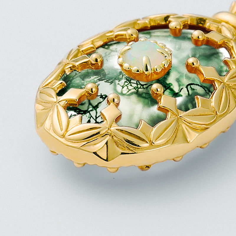 Gold - toned necklace: Oval moss agate pendant with central opal, decorative frame, isolated on white focusing on details