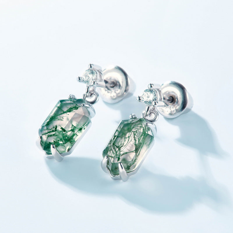 Silver drop earrings featuring moss agate, cubic zirconia studs, close - up on light blue background