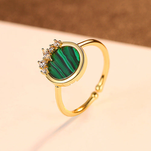 Gold ring with a green malachite gemstone on a beige background