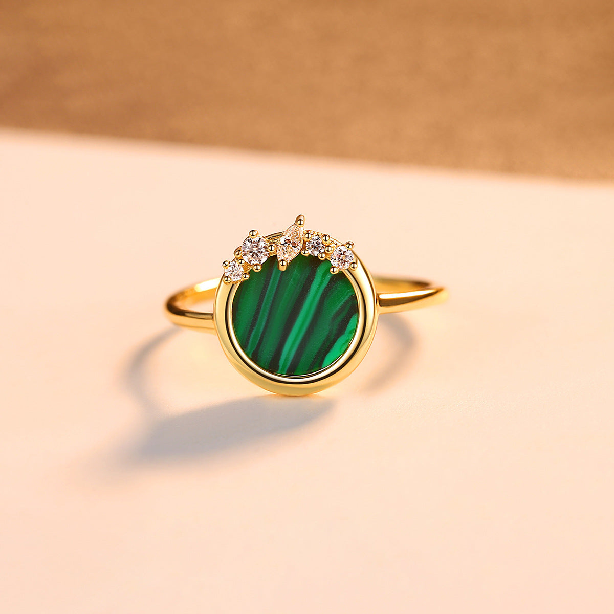 Gold ring with a green malachite gemstone and small CZ cluster on a beige background