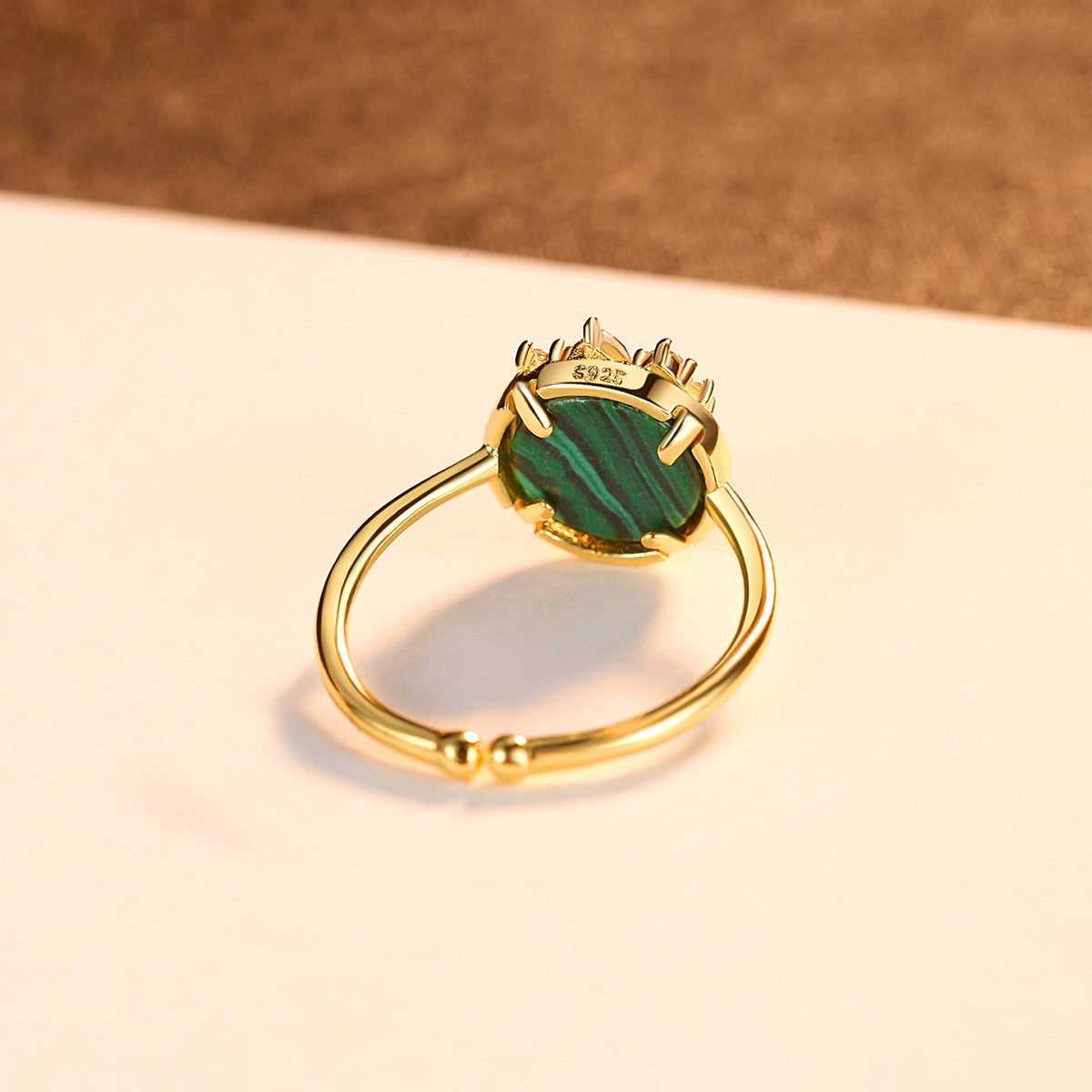 Gold ring with a green gemstone with adjustable open band on a beige surface