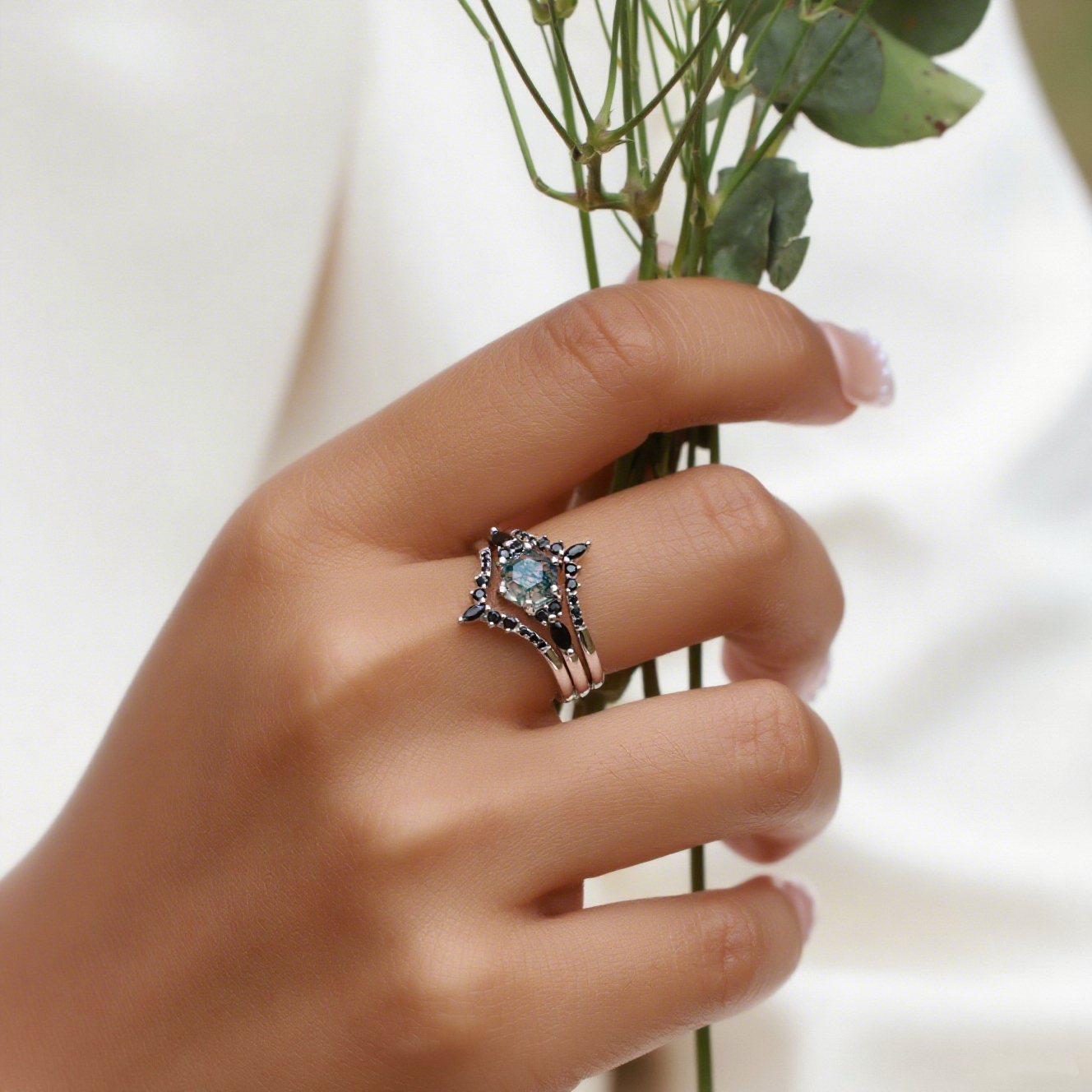 Silver - toned ring set with hexagonal moss agate, black gemstone accents, worn on a hand holding greenery.
