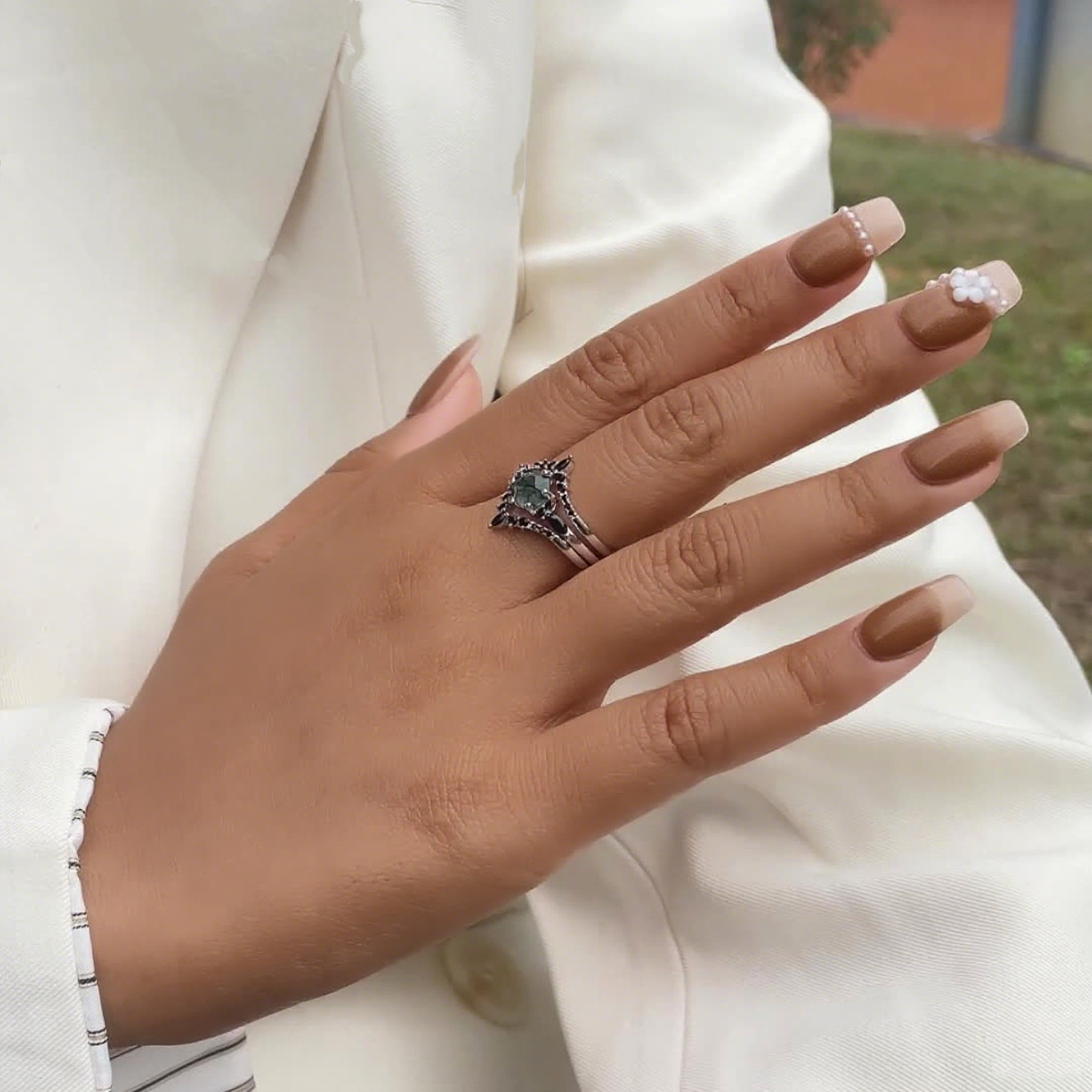 Hands wearing silver - toned ring set: Hexagonal moss agate ring with black gemstone decorations, against a white jacket.