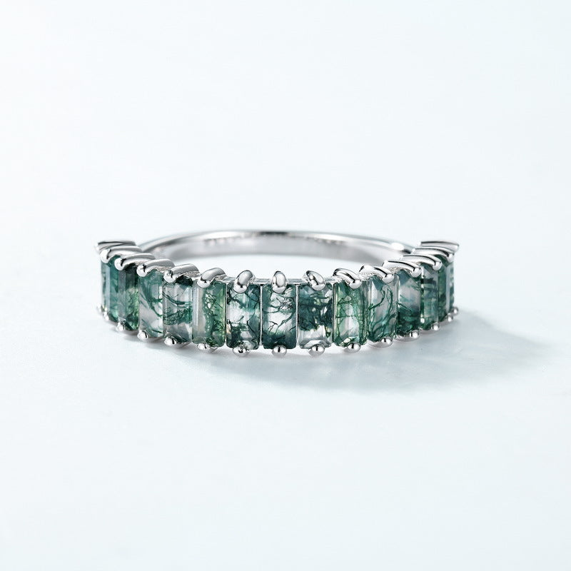 Silver ring featuring a moss agate eternity - band design, shown in close - up on a light blue backdrop, emphasizing craftsmanship and stone details.