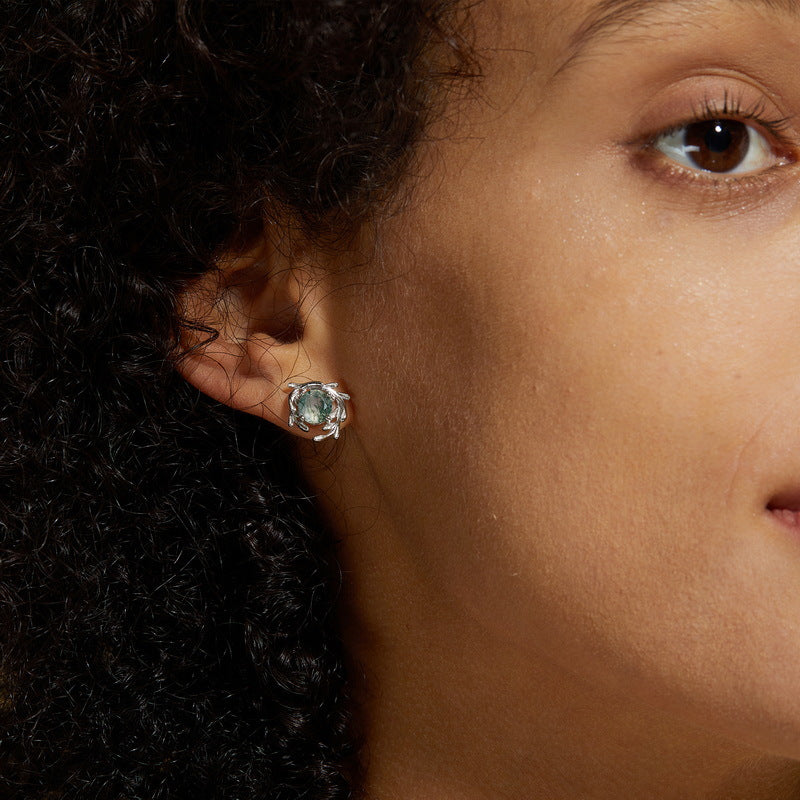 Close - up of silver - toned earring on a person: Leafy branch frame, round moss agate stone, showcasing elegant style.