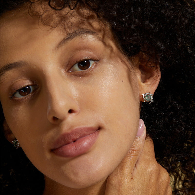 Close - up of a person wearing silver - toned earrings: Leafy branch frames, round moss agate stones, highlighting the jewelry.