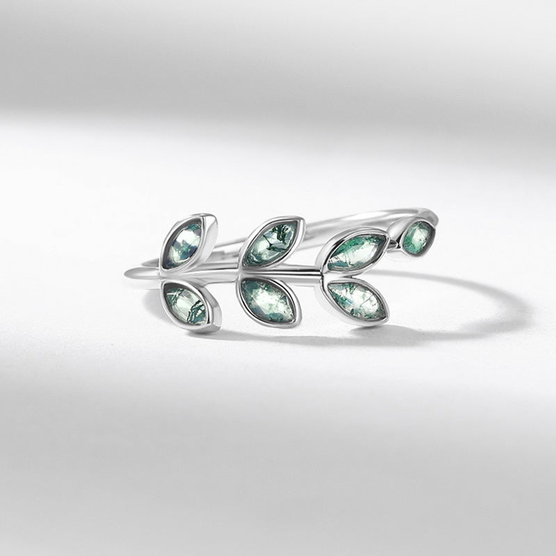 Silver ring featuring leaf - branch design, moss agate accents, close - up on light gray background, emphasizing details