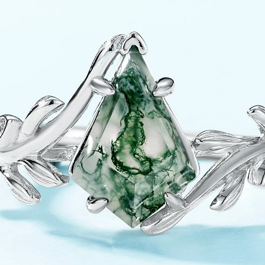 Extreme close - up of silver ring: Diamond - shaped moss agate, leaf - branch details, on light blue.