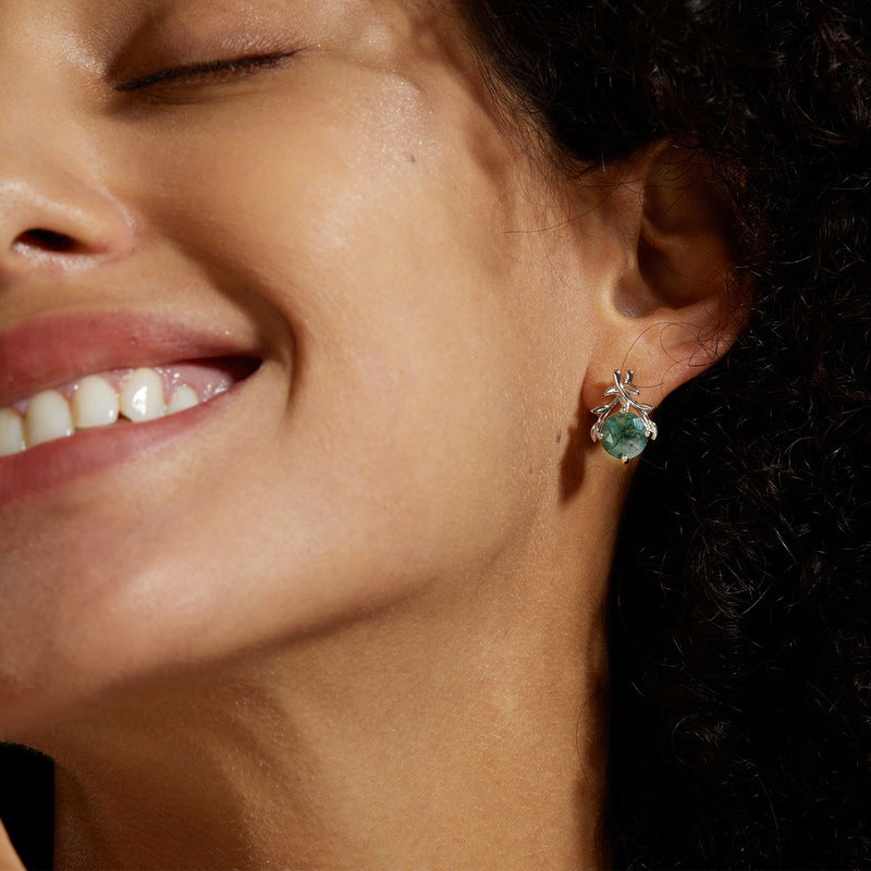 Close - up of silver earrings on a person: Round moss agate with leaf - branch details.