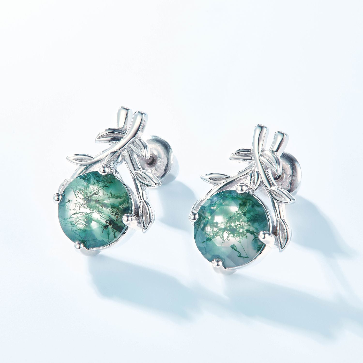 Silver earrings: Round moss agate with leaf - branch design, on a light blue background.