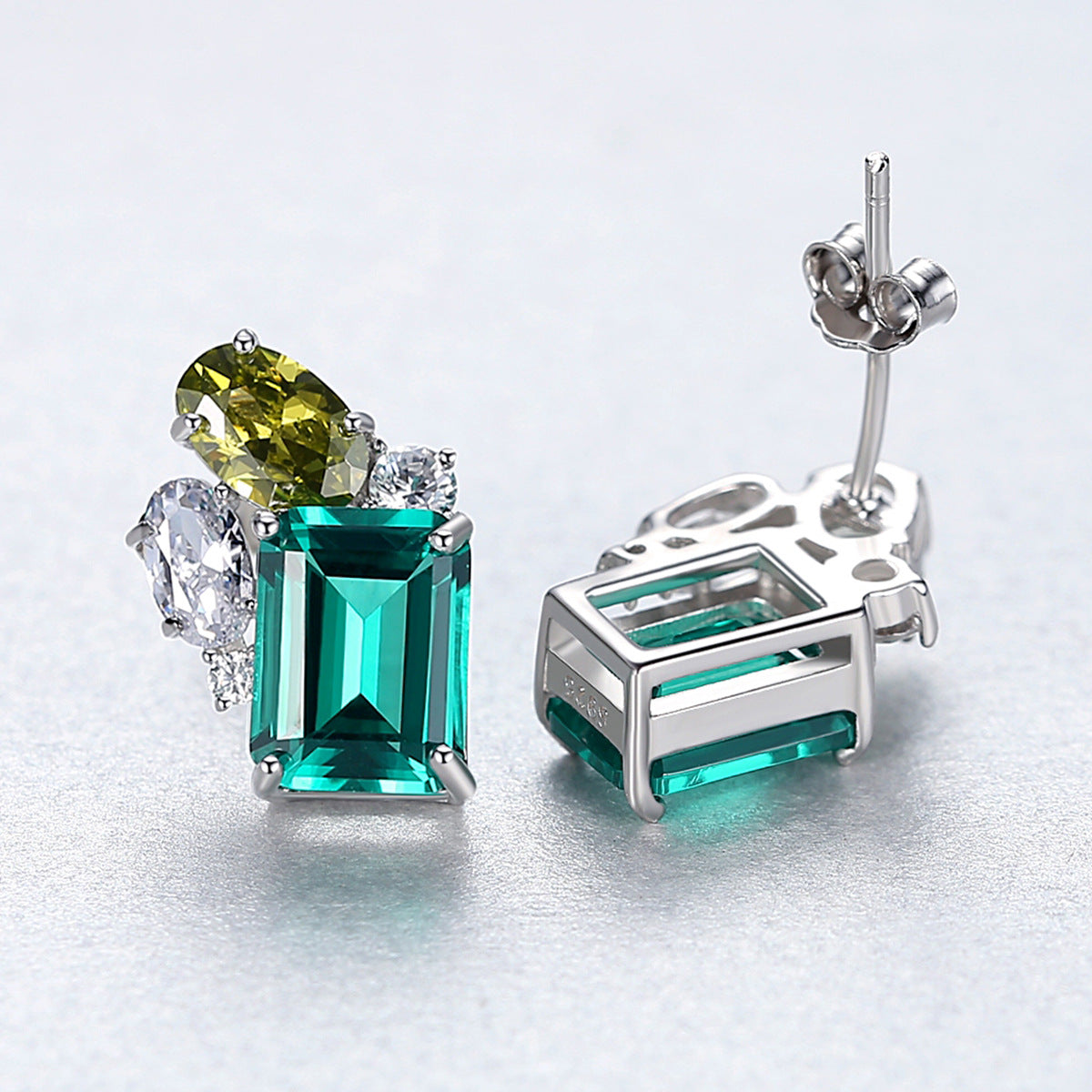 Pair of earrings with green gemstones on a light gray background one showing the face and the other one showing the back