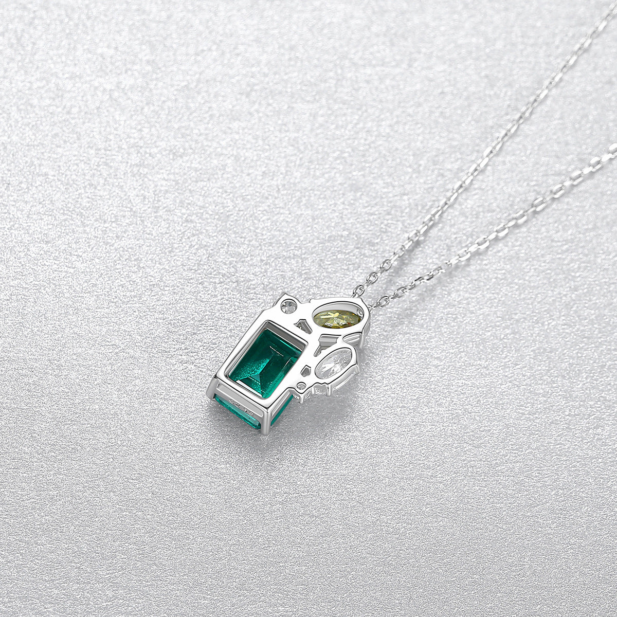 Silver pendant with green gemstone from the back on a light gray background