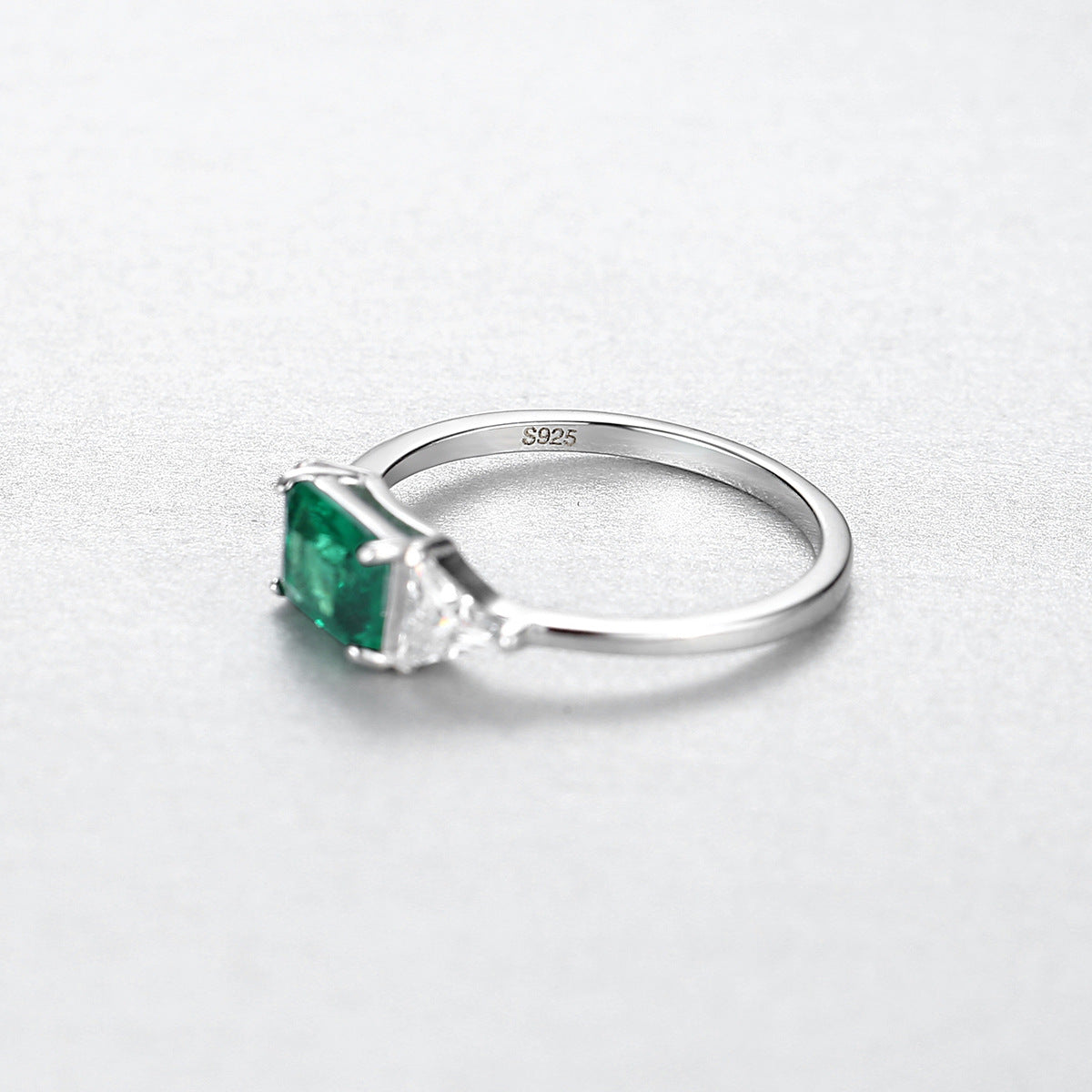 Silver ring with a green gemstone with S925 stamp on a light gray background