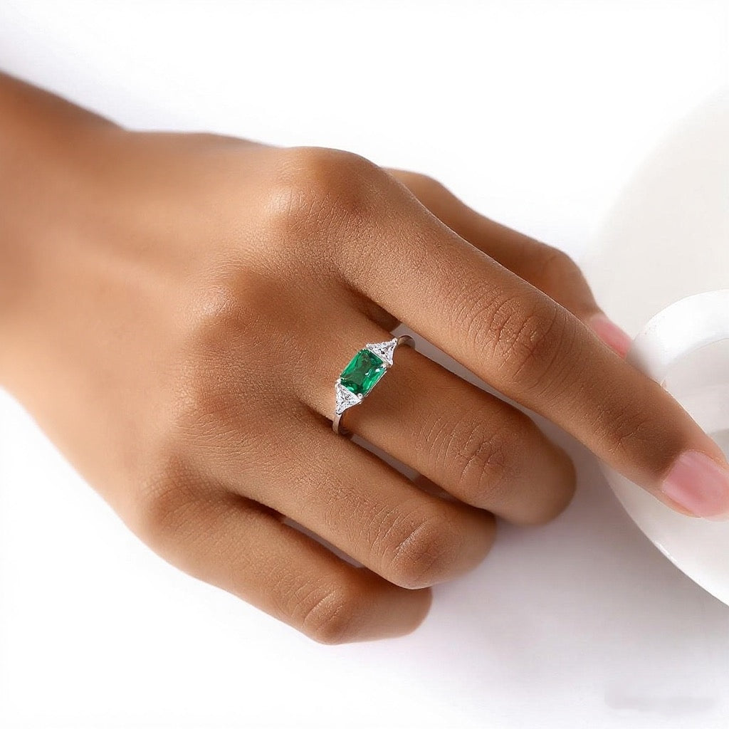 Hand wearing a ring with an emerald stone on a white background